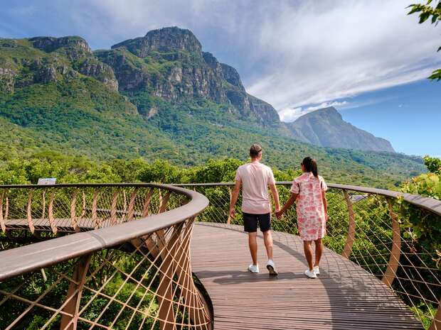 A couple walking along the Boomslang Walkway, a canopy bridge above foliage in Kirstenbosch Botanical Garden in Cape Town.